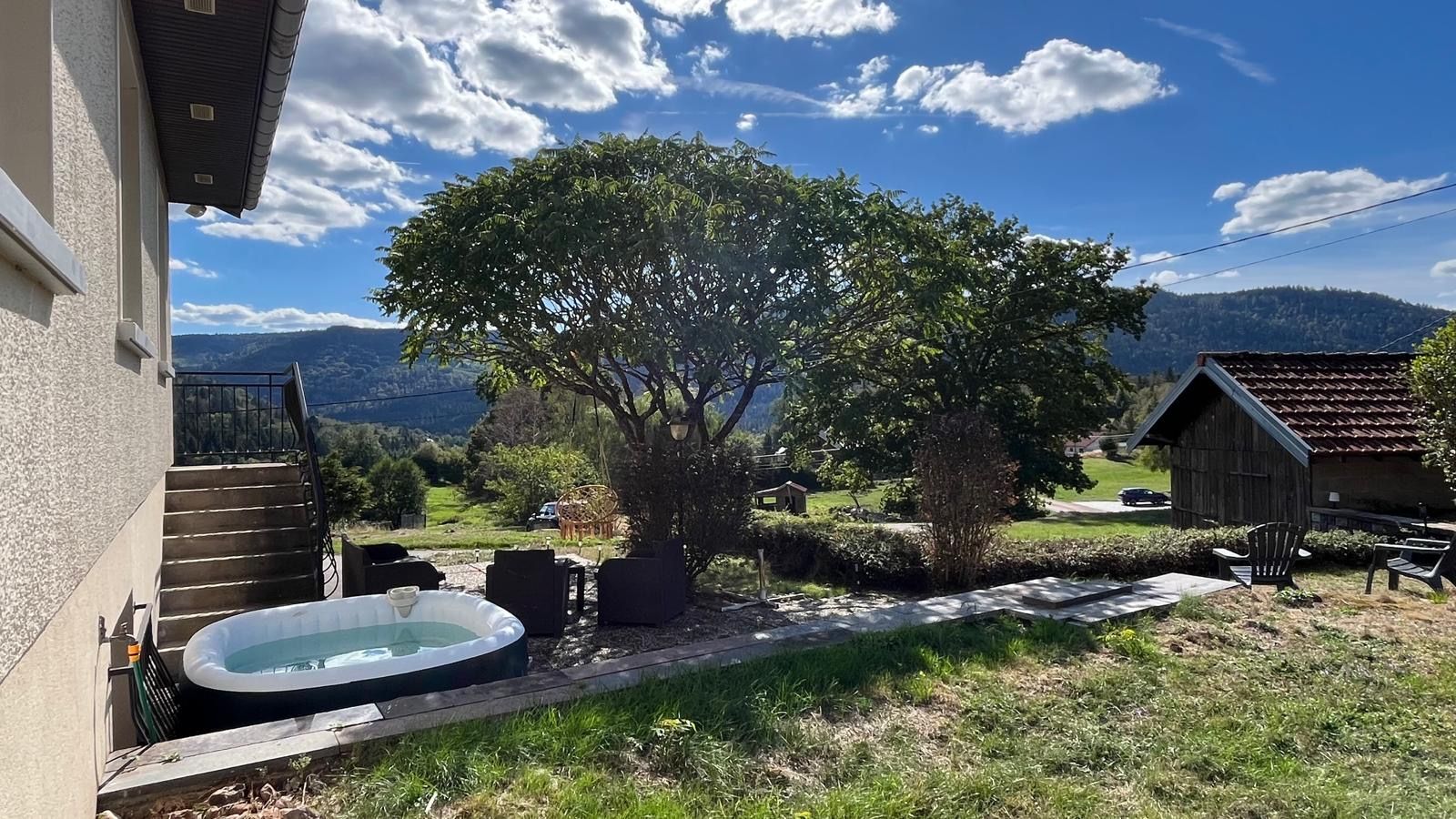 Un jardin avec un jacuzzi, un espace salon extérieur, un arbre et une vue sur les montagnes.