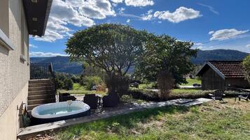 Un jardin avec un jacuzzi, un espace salon extérieur, un arbre et une vue sur les montagnes.