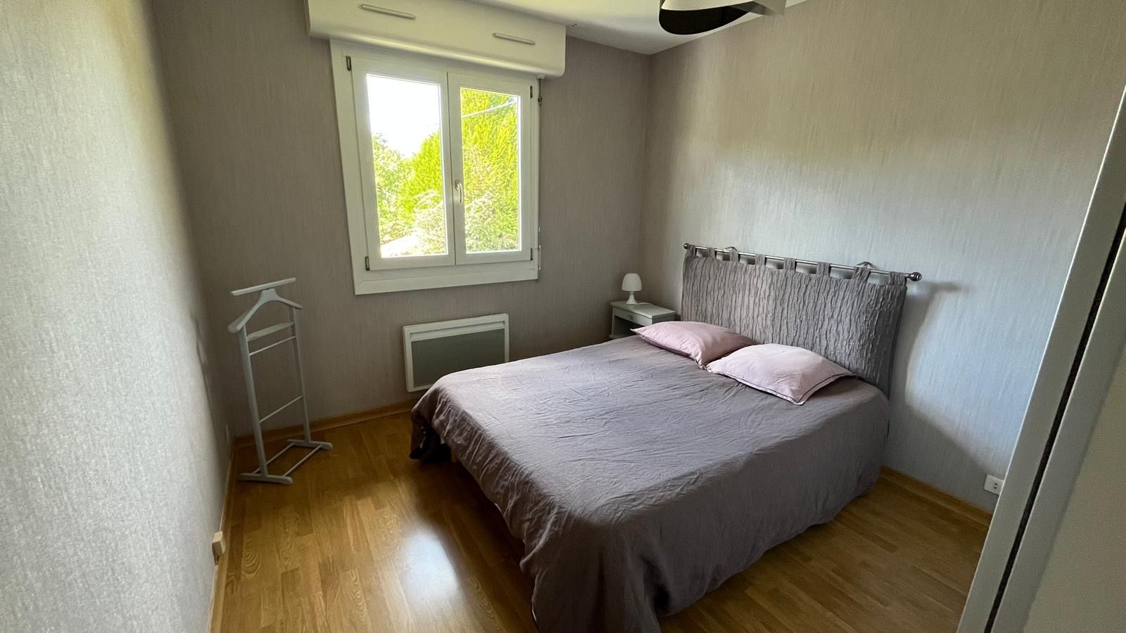 Un dormitorio con cama, ventana, radiador y mesita de noche.