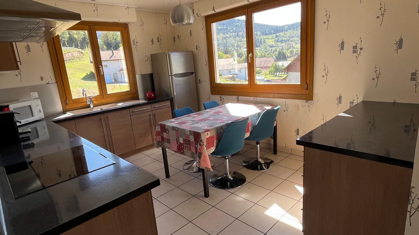 Een keuken met een eettafel, stoelen, een koelkast en een raam met uitzicht.