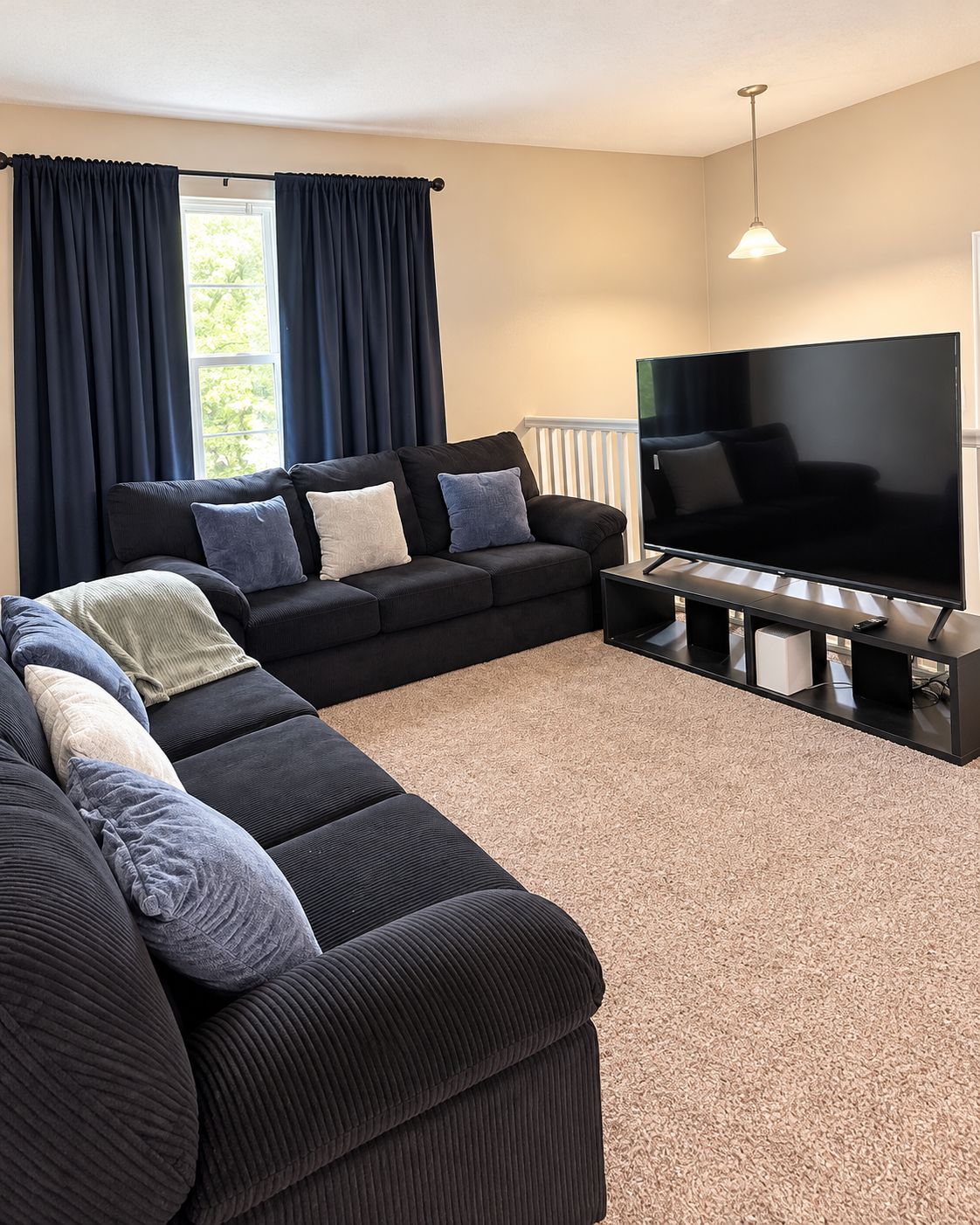 A living room with a sectional sofa, a flat-screen TV, and a window with curtains.