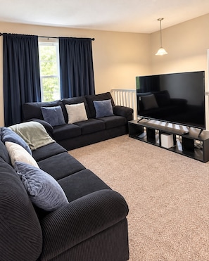 A living room with a sectional sofa, a flat-screen TV, and a window with curtains. - Serene 3-bedroom 2-bath house (Omaha)