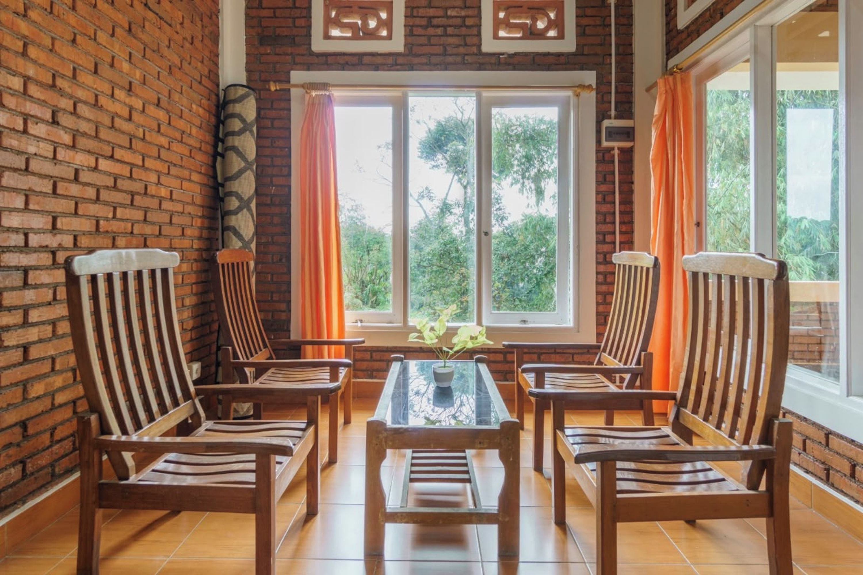 A room with a brick wall, a glass table with chairs, and large windows with curtains.