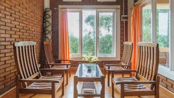 A room with a brick wall, a glass table with chairs, and large windows with curtains.