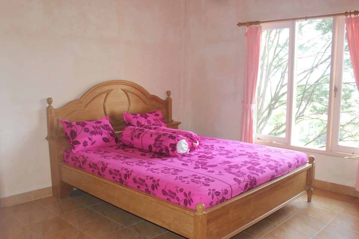 Ein Einzelbett mit Holz Kopfteil und floralem Bettbezug in einem Zimmer mit Fenster und rosa Vorhängen.