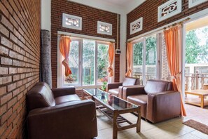 A living room with brick walls, leather sofas, a glass coffee table, and large windows with curtains. - Villa Insani Syariah (Bogor)