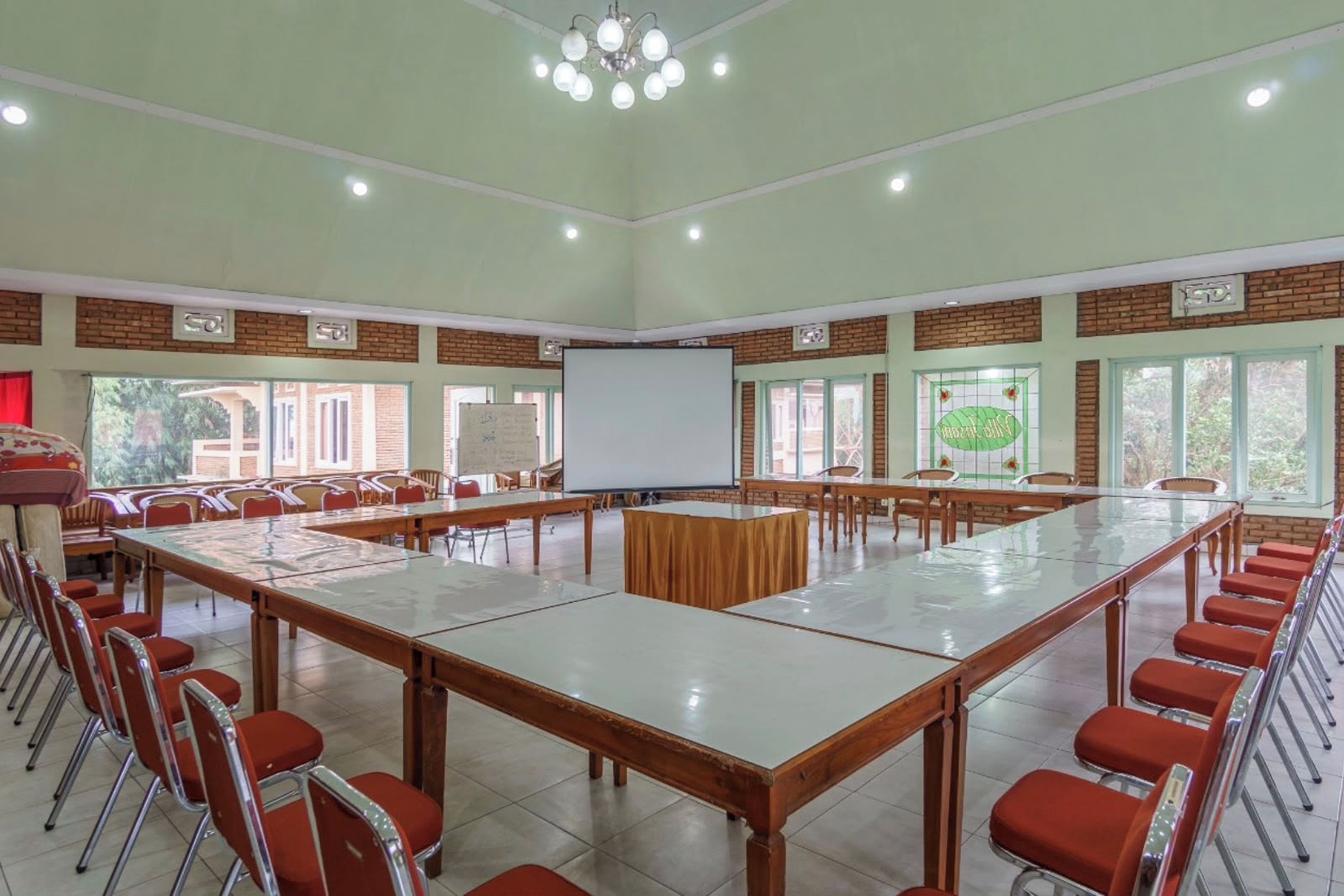 A conference room with a long table, red chairs, a projector screen, and large windows.