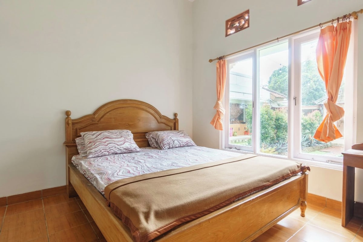 Ein Zimmer mit einem Holzbett, einem Vorhangfenster und Blick auf Grünfläche.