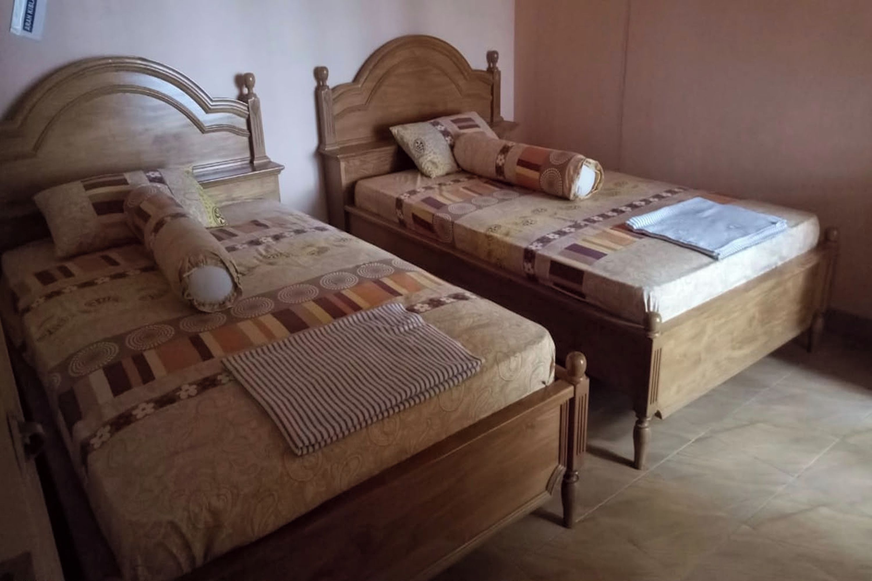 Two wooden beds with headboards, a patterned bedspread, and a rolled-up blanket on the floor.