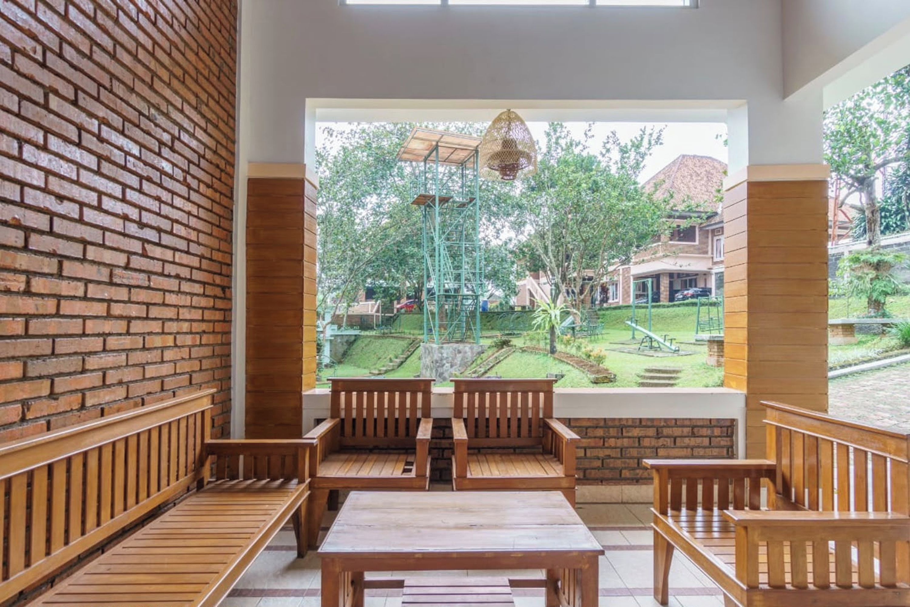 A room with a brick wall, wooden benches, and a view of a garden with playground equipment.
