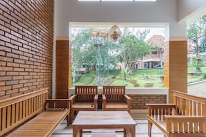 A room with a brick wall, wooden benches, and a view of a garden with playground equipment. - Villa Insani Syariah (Bogor)
