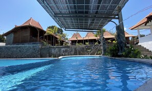 Una piscina con pared de piedra y un área techada con techo metálico.