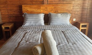 Una cama con cabecera de madera, ropa de cama gris y dos mesitas de noche de madera.