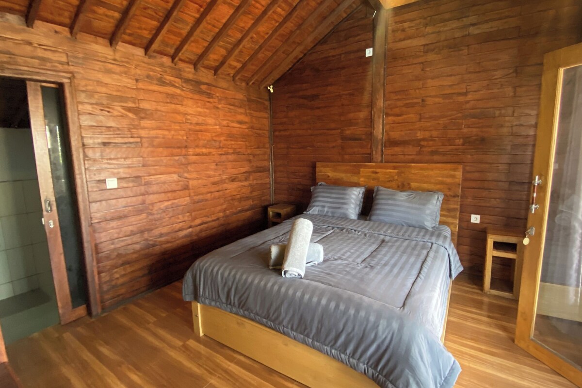Una habitación de madera con una cama, una mesita de noche y una puerta.