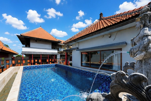 A swimming pool with a tiled deck, a building with a tiled roof, and a decorative stone sculpture. - Ava Guest House Bali (Ungasan)