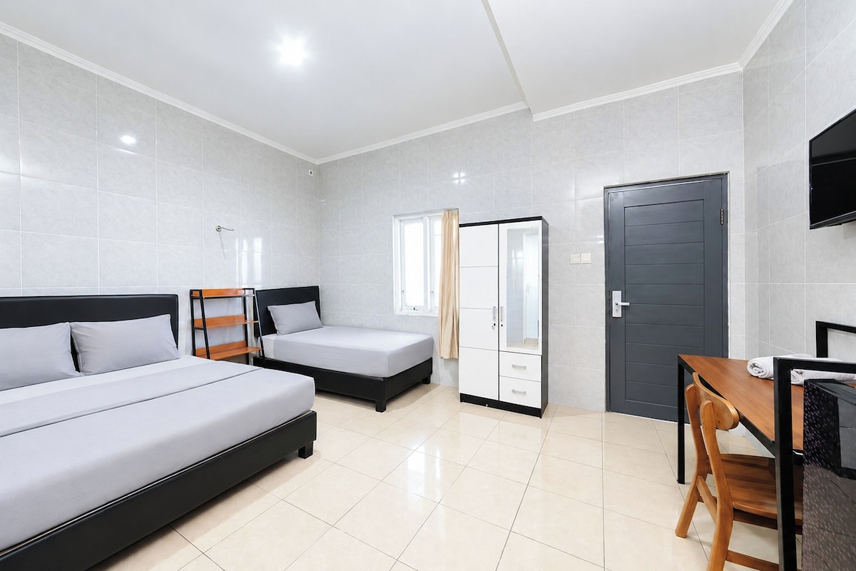 A hotel room with two beds, a desk, a chair, a wardrobe, and a TV.