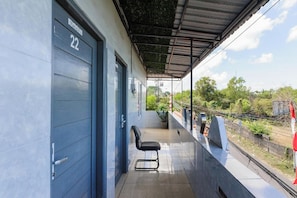 A covered outdoor area with a single chair, a blue garage door marked with the number 22, and a view of greenery and a fence in the background. - Ava Guest House Bali (Ungasan)