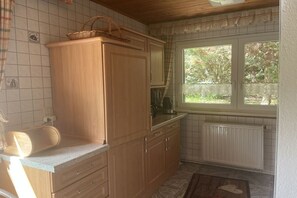 A kitchen with wooden cabinets, a countertop, a window with a view of greenery, and a radiator. - Holiday home with 1 bedroom (Blankenburg \/ Wienrode)