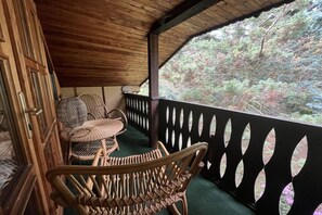 A wooden balcony with wicker furniture and a view of a forested area. - Holiday home with 1 bedroom (Blankenburg \/ Wienrode)