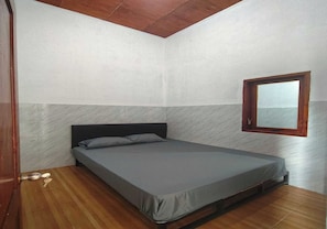 Ein Schlafzimmer mit einem Einzelbett, Holzboden und einem Fenster mit Holzrahmen.