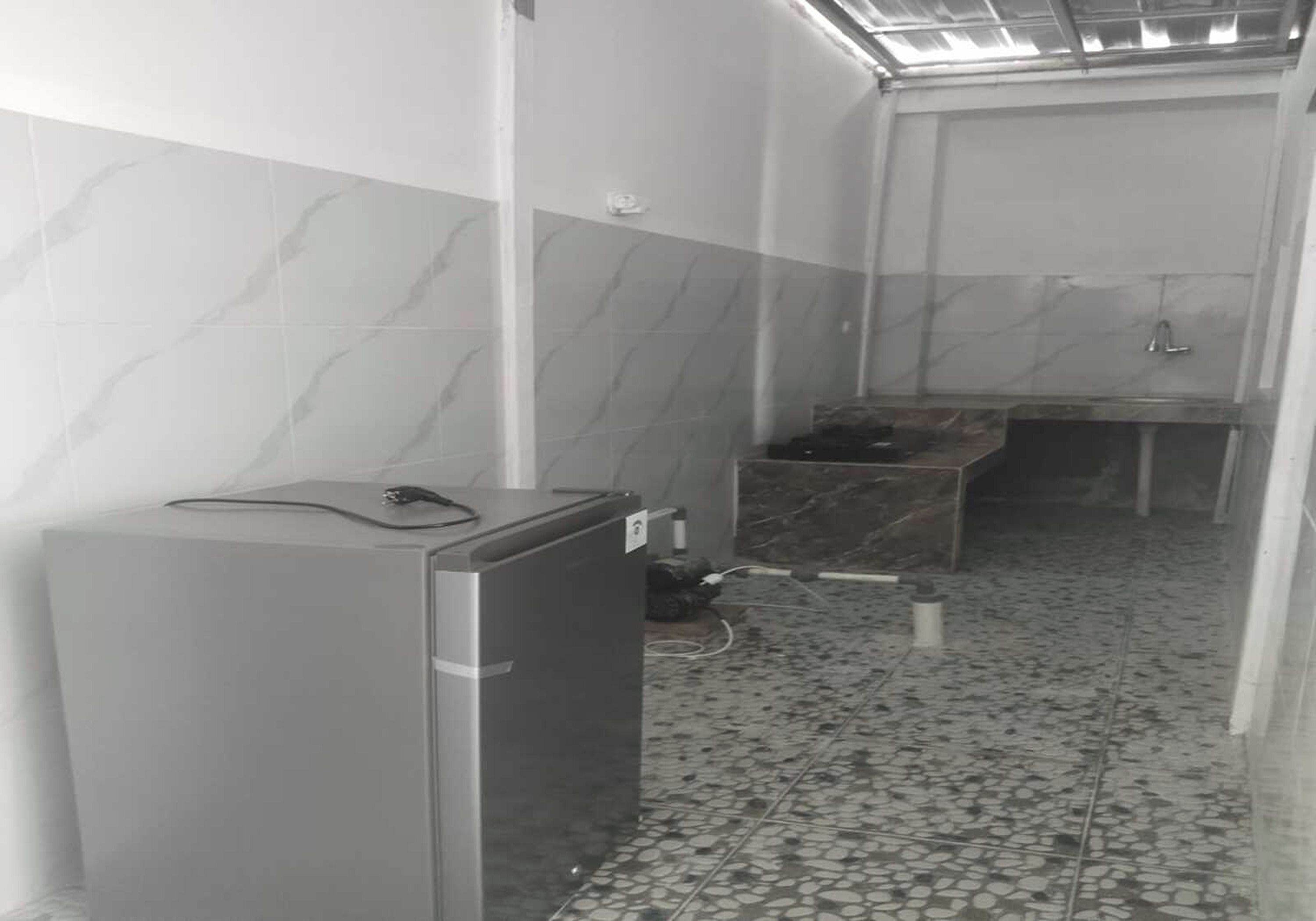 A narrow hallway with a tiled floor, a small refrigerator, and a sink area.