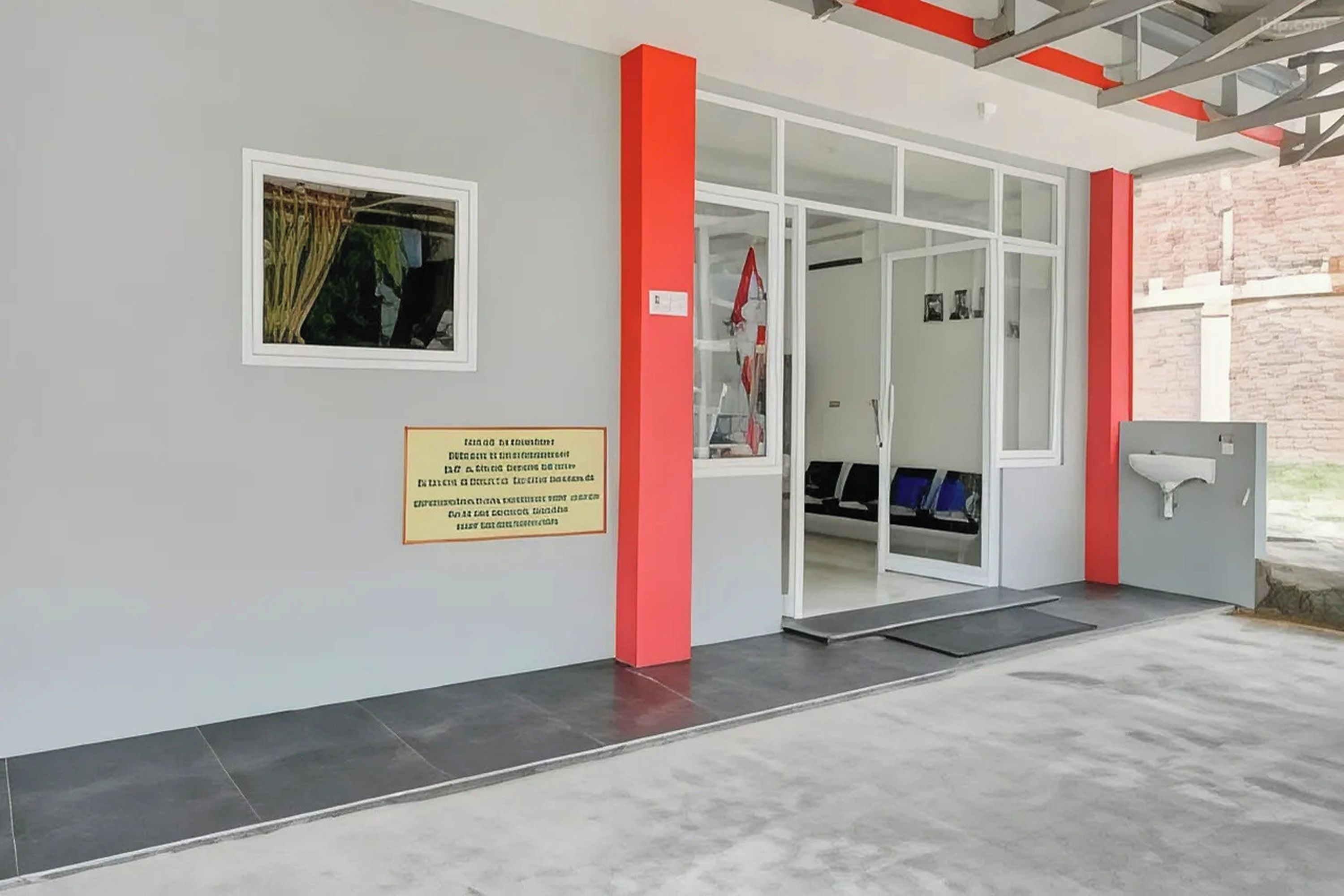A building entrance with a glass door, a wall-mounted sign, and a small window with a view of outdoor plants.