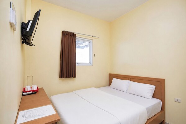 A single bed with white bedding, a wooden headboard, a small table with a red tray, a wall-mounted TV, and a window with brown curtains.