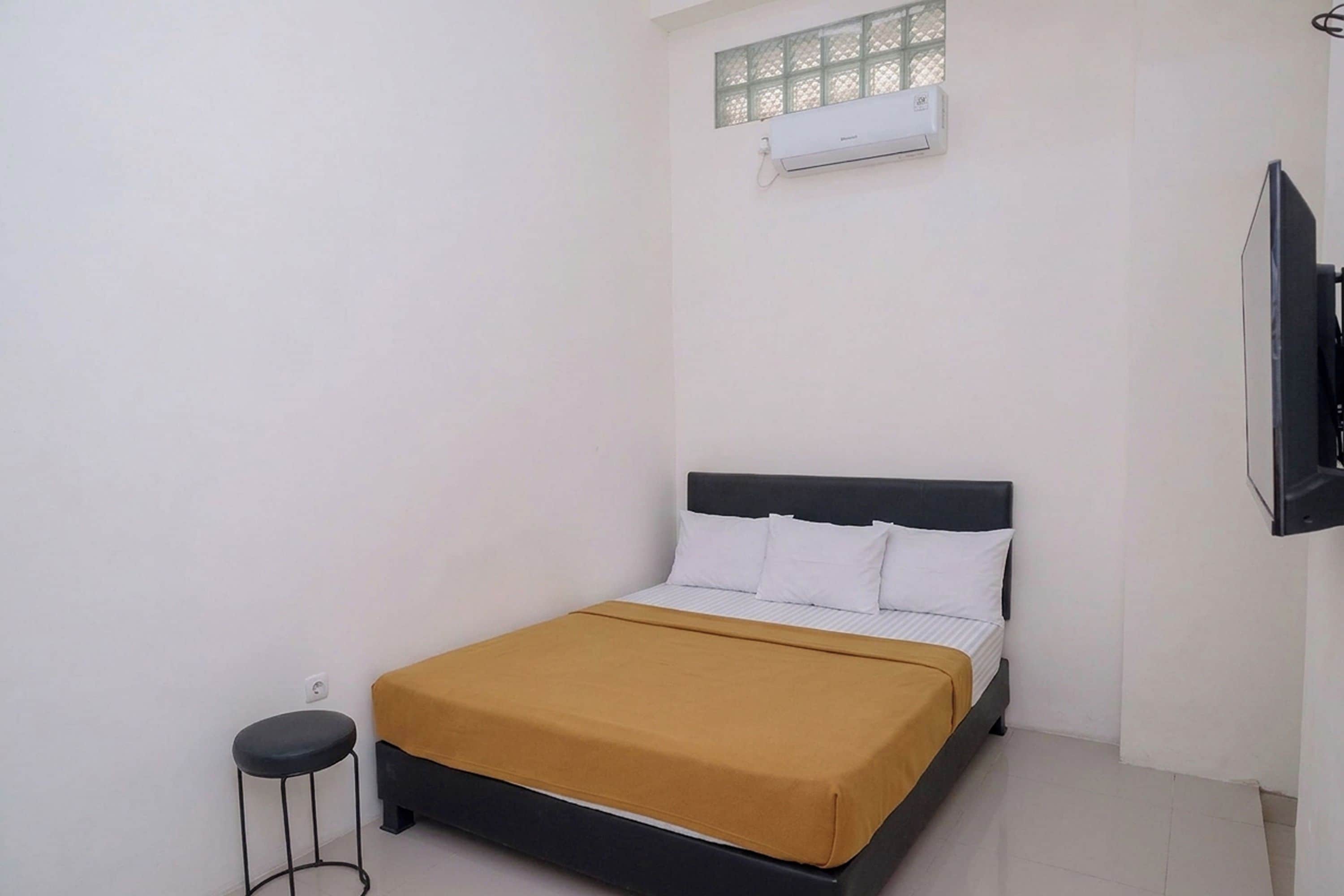 A single bed with a black headboard and white bedding, a small stool, and a wall-mounted air conditioning unit.