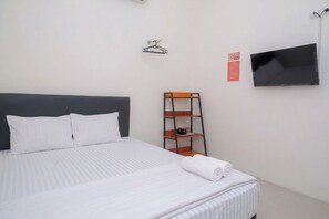 A hotel room with a bed, a TV mounted on the wall, and a wooden shelf unit. - Ava Guest House Magelang (Magelang)