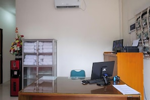 A reception desk with a computer, a telephone, and a small blue chair. There is a glass display case with folded towels and a red vending machine.