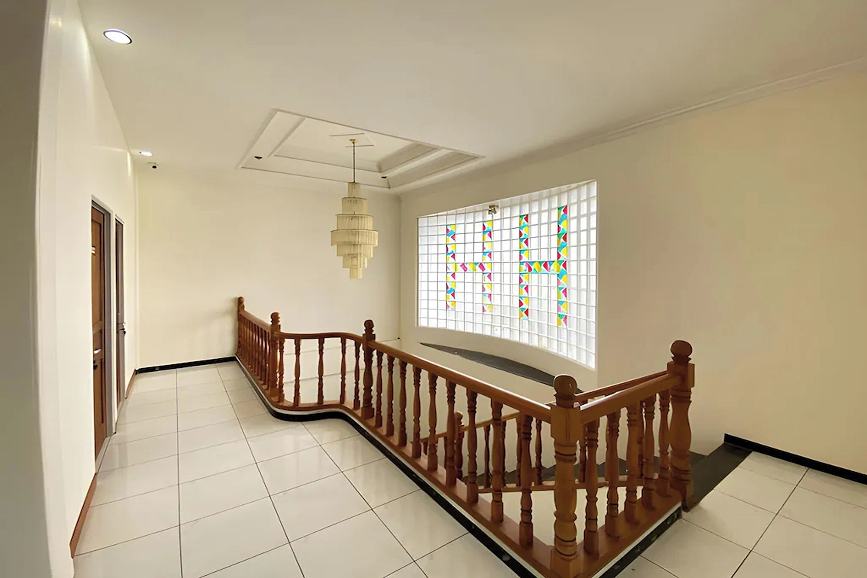 A staircase with wooden balusters and a handrail, leading to a landing with a ceiling fan and a window with a grid pattern.