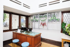 A reception desk with a wooden finish, two blue cushioned stools, and a glass-top table. - Ava Hotel Bayeman Tidar (Magelang)