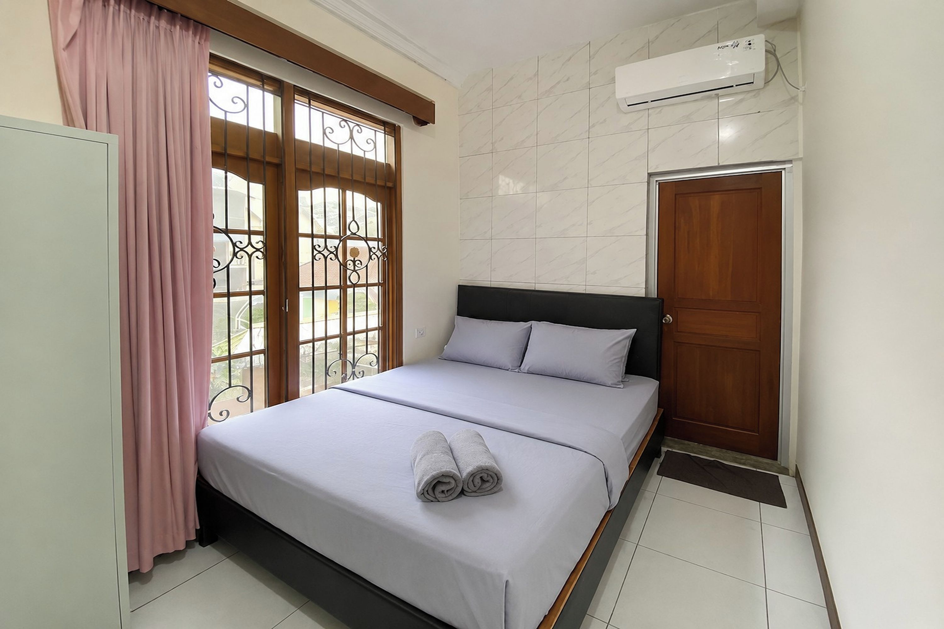 Une chambre à coucher avec un lit, une fenêtre avec des barreaux en métal, une porte et un appareil de climatisation.