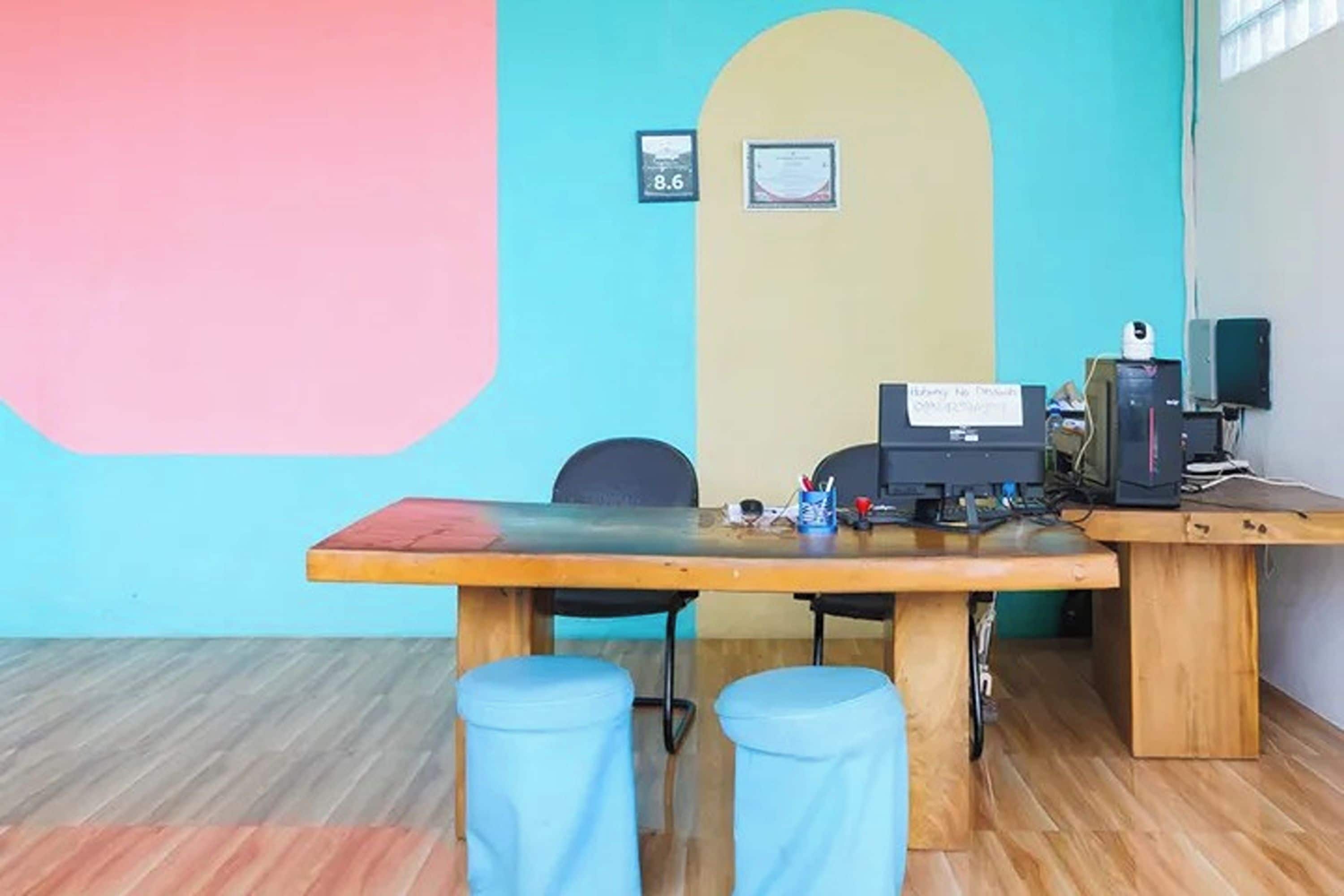Een kamer met een groot bureau, computer en twee blauwe krukken. Twee ingelijste certificaten hangen aan de muur.