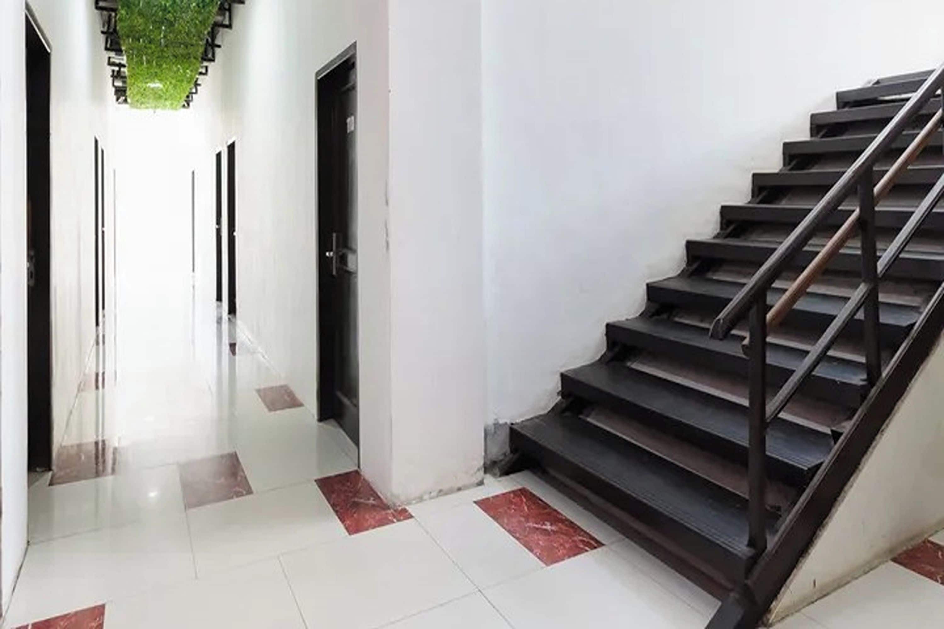 A hallway with a staircase leading to an upper floor. The floor is tiled with a pattern of white and red tiles.