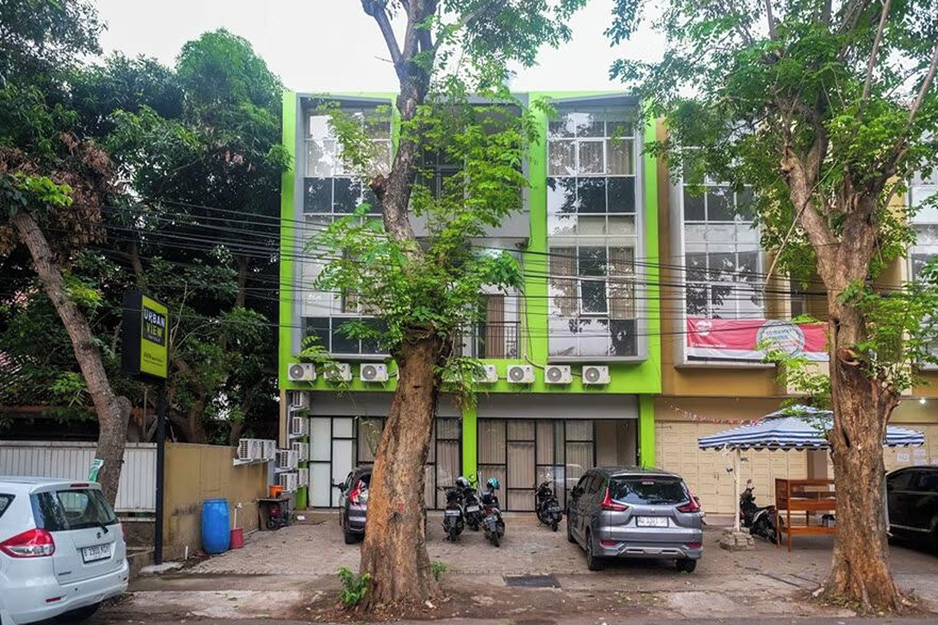 Um edifício com várias andares, fachada verde, carros estacionados e árvores na frente.