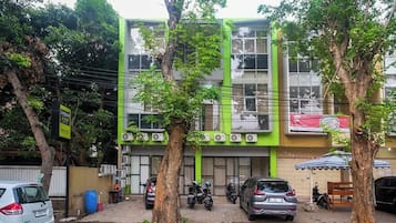 Um edifício com várias andares, fachada verde, carros estacionados e árvores na frente.