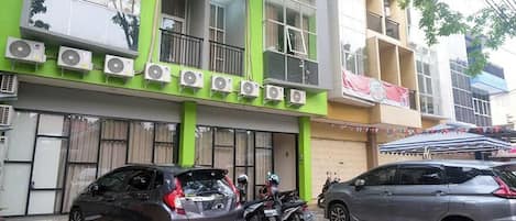 A multi-story building with air conditioning units on the facade, a motorcycle parked in front, and a car parked to the side.