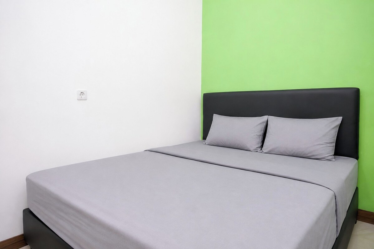 Uma cama de solteiro com colchão e almofadas cinzas, cabeceira preta e parede verde.