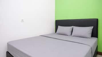 Uma cama de solteiro com colchão e almofadas cinzas, cabeceira preta e parede verde.