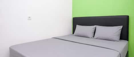 Uma cama de solteiro com colchão e almofadas cinzas, cabeceira preta e parede verde.