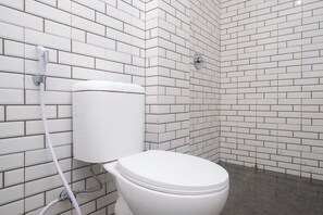 Sanitário com vaso branco, chuveiro e parede revestida em azulejo.
