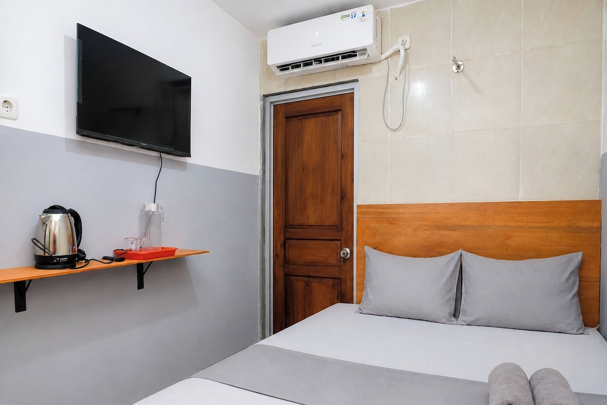 A hotel room with a bed, a television mounted on the wall, a coffee maker, and a water dispenser on a shelf.