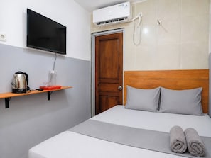 A hotel room with a bed, a television mounted on the wall, a coffee maker, and a water dispenser on a shelf.
