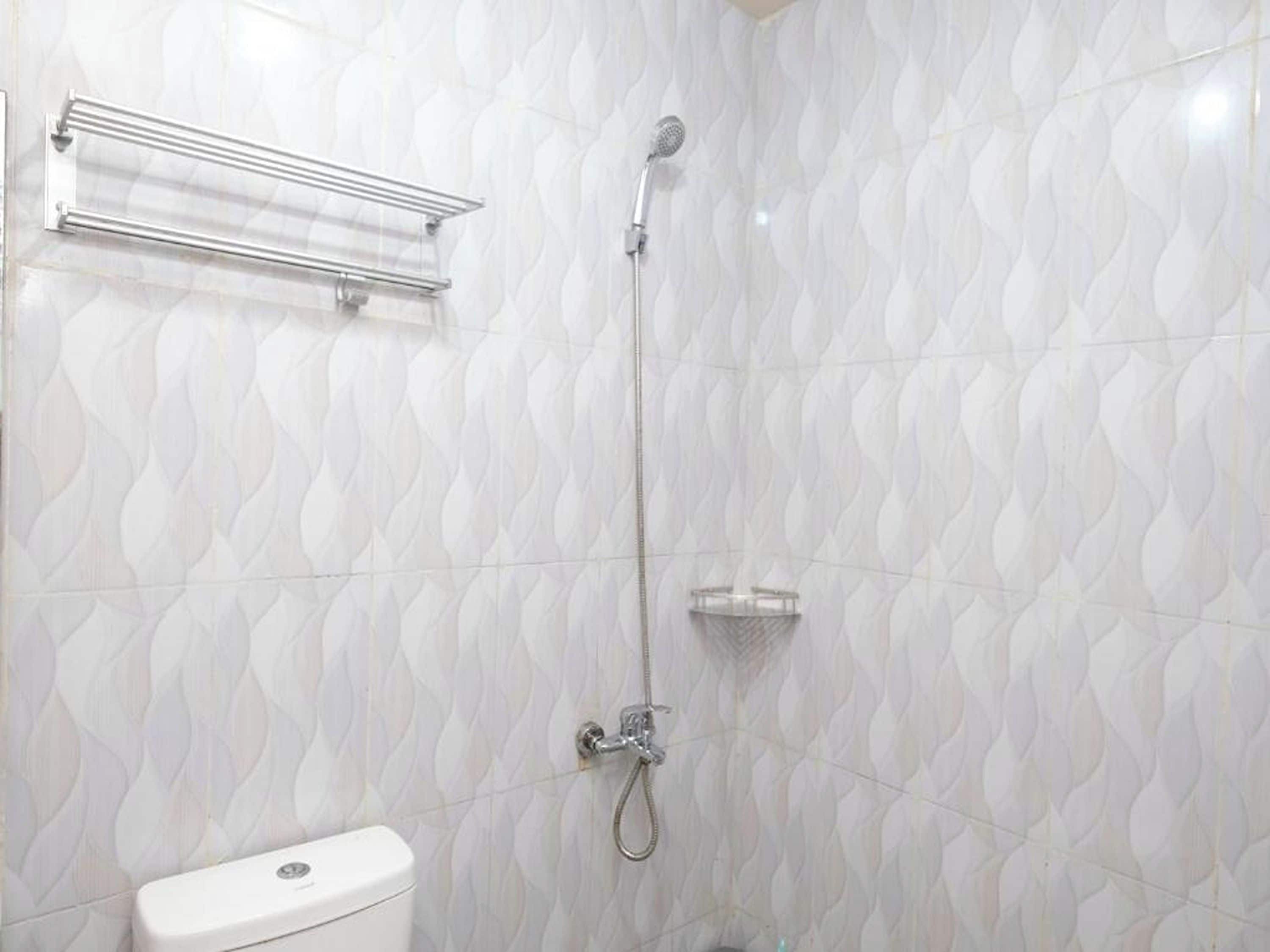 Un baño con inodoro, ducha con cabezal de ducha manual y barra para toallas.