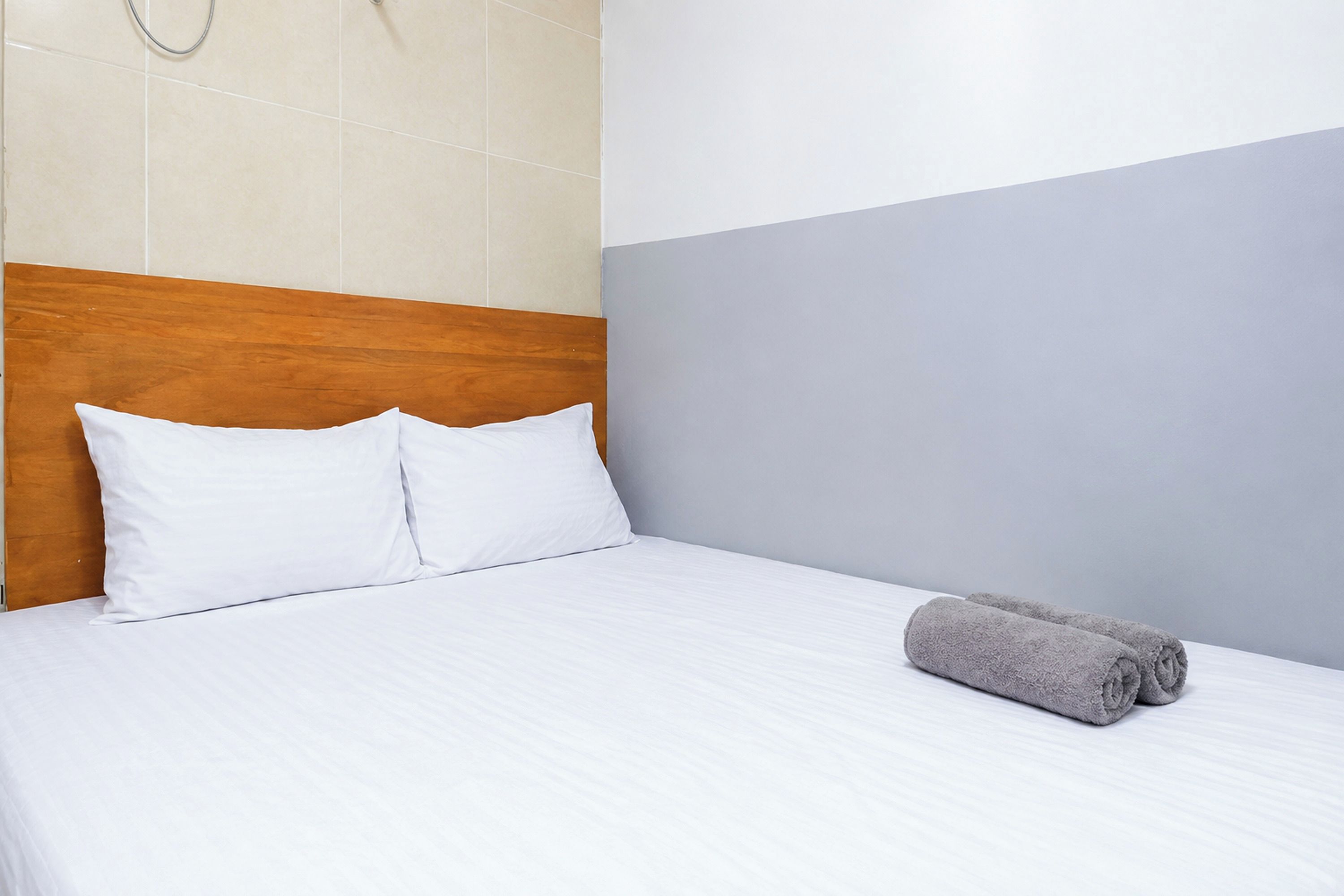 Habitación de hotel con cabecera de madera, cama con ropa blanca y una toalla gris enrollada sobre la cama.