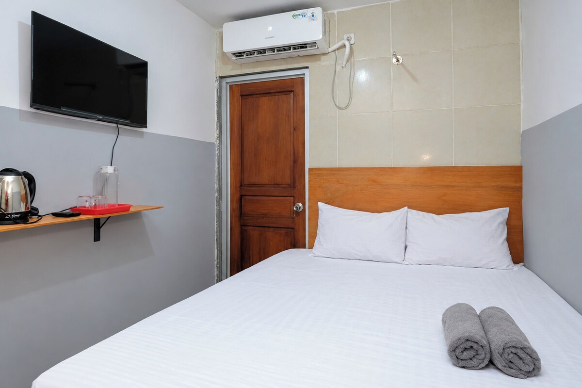 Una habitación de hotel con una cama, un televisor montado en la pared, un aire acondicionado y una puerta de madera.