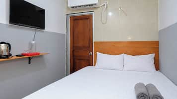 Una habitación de hotel con una cama, un televisor montado en la pared, un aire acondicionado y una puerta de madera.