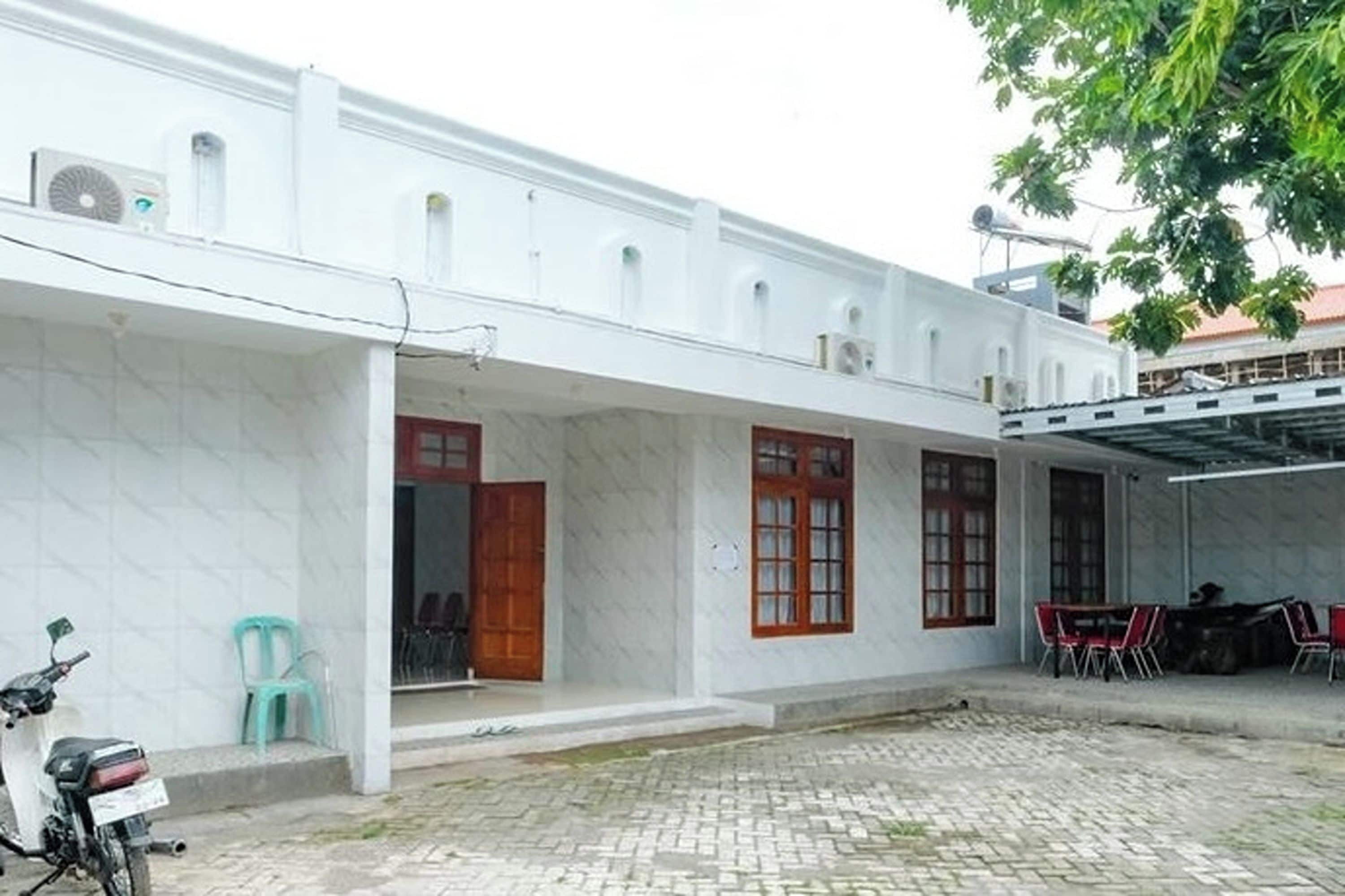 A white building with a covered patio area, a motorcycle parked outside, and a paved courtyard.