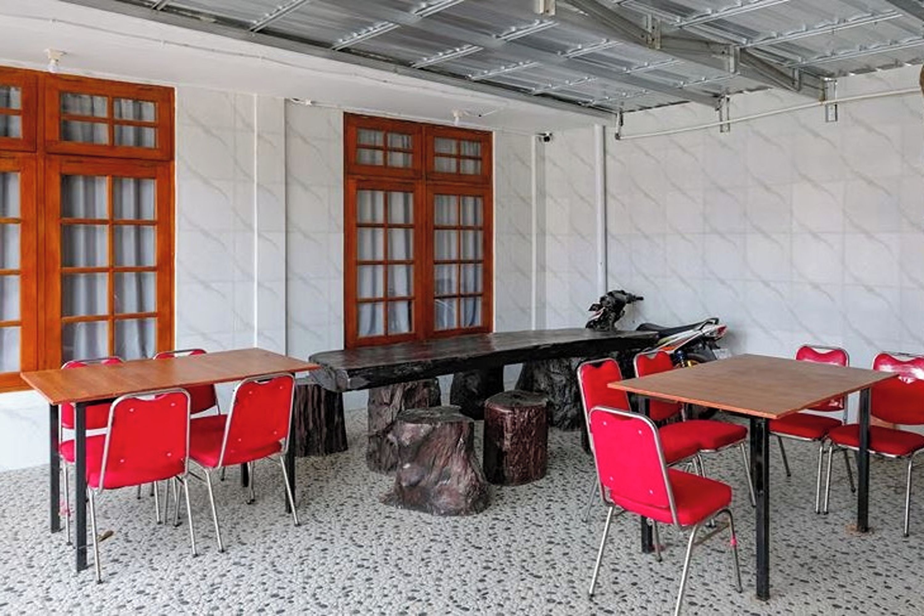 Un salón de conferencias con una gran mesa de madera rodeada de sillas rojas, una motocicleta y un taburete de madera.